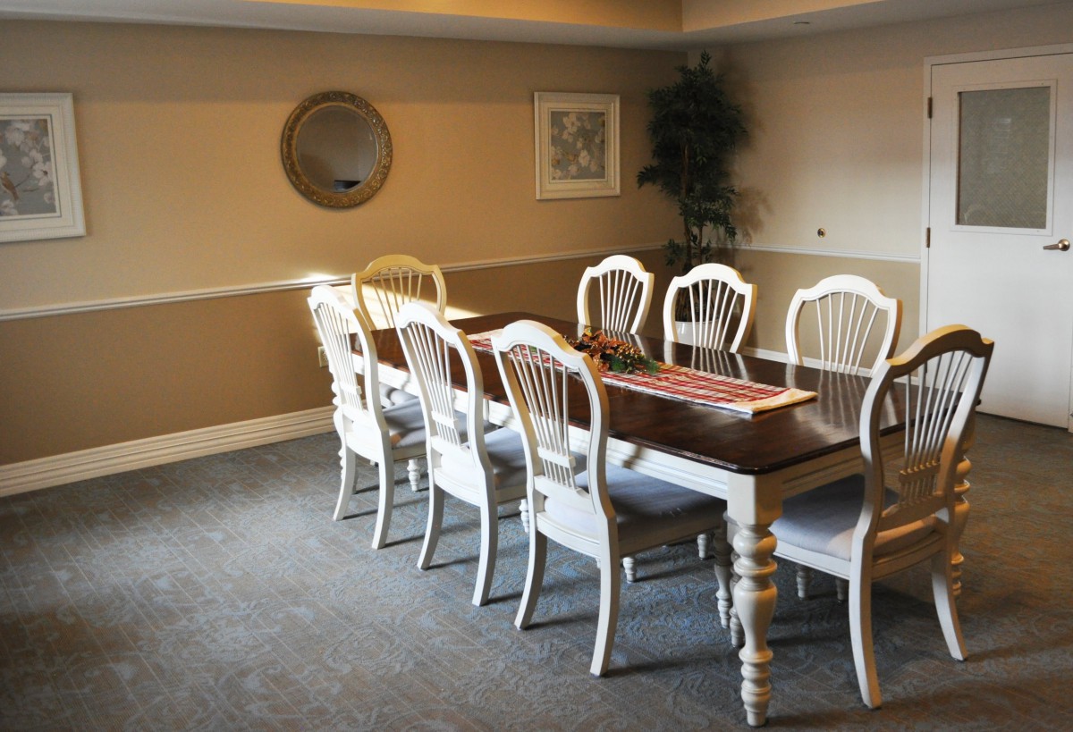 A neatly arranged dining room with a long table and eight chairs, featuring wall decorations and a mirror.