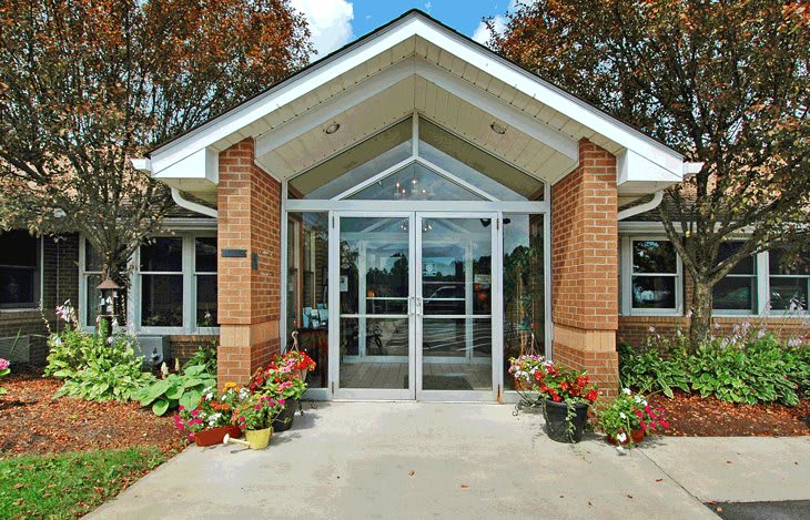 A modern building entrance with brick pillars and glass doors, surrounded by plants and landscaping.