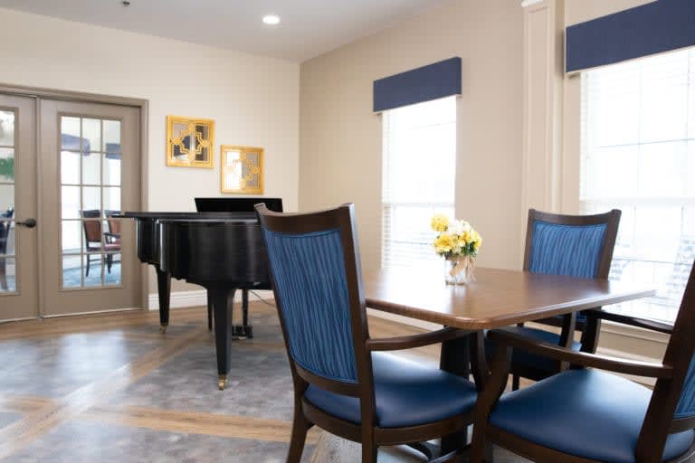 A cozy room featuring a grand piano and a dining table with blue upholstered chairs.