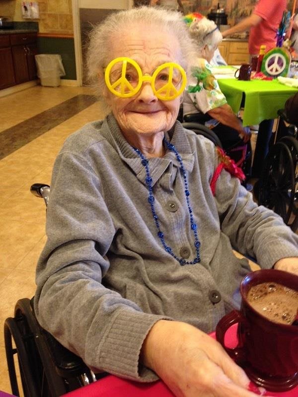 An elderly person wearing peace sign glasses enjoys a drink, embracing a fun and colorful atmosphere.