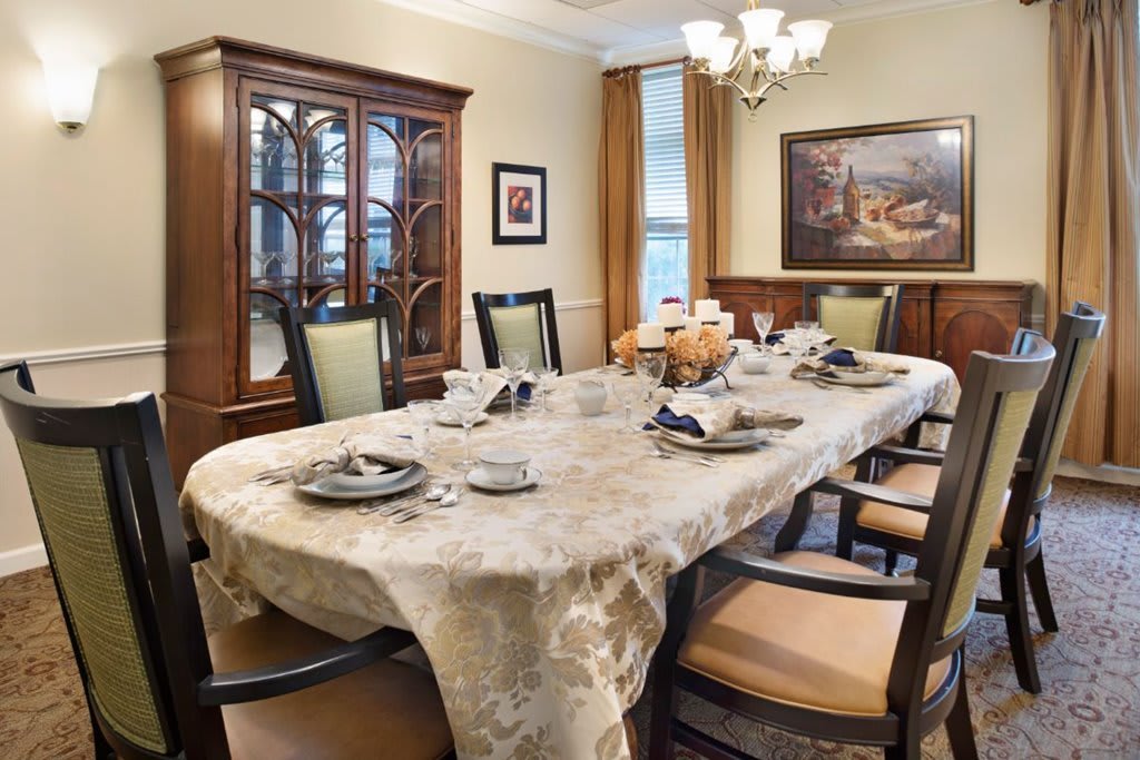 An elegant dining room with a table set for a meal, featuring a decorative tablecloth and matching chairs.
