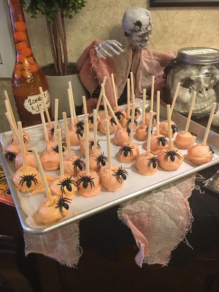 Halloween-themed cake pops with orange frosting and spider decorations.