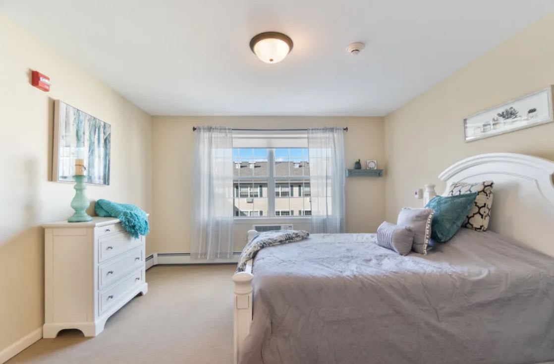 A bright and cozy bedroom featuring a bed, dresser, and large window.