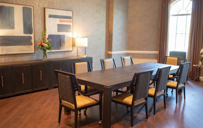 A well-furnished dining room with a large table, several chairs, a sideboard with a lamp, and wall artwork.