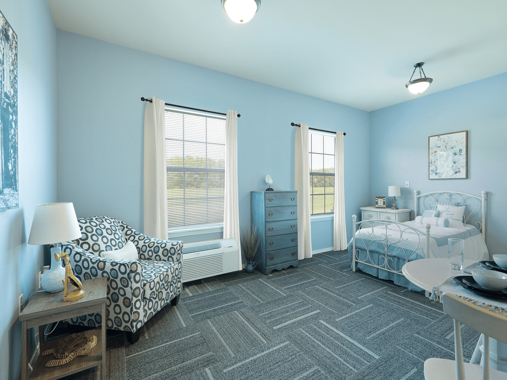 A bright and inviting bedroom with twin beds, blue walls, natural light, and cozy furnishings.