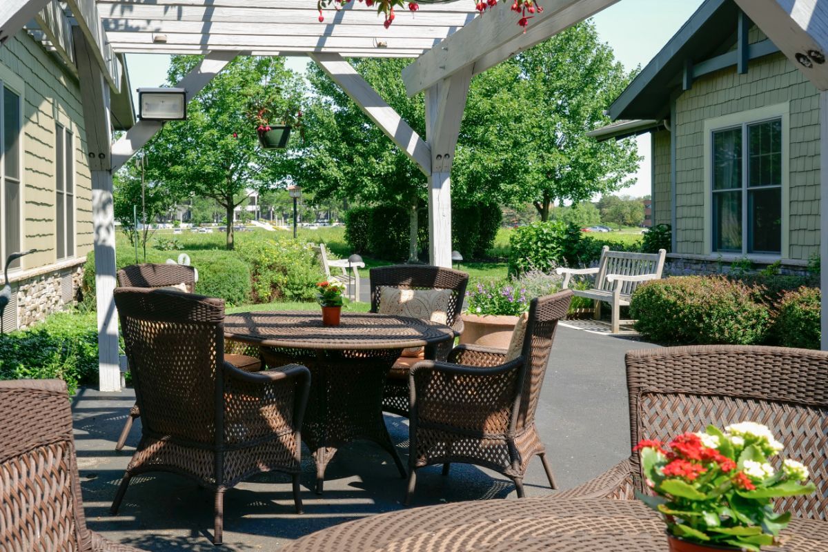 A cozy outdoor patio area with wicker furniture under a pergola, surrounded by greenery.