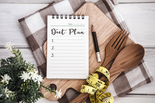 A tidy diet plan notebook ready for meal planning with wooden utensils and a tape measure.