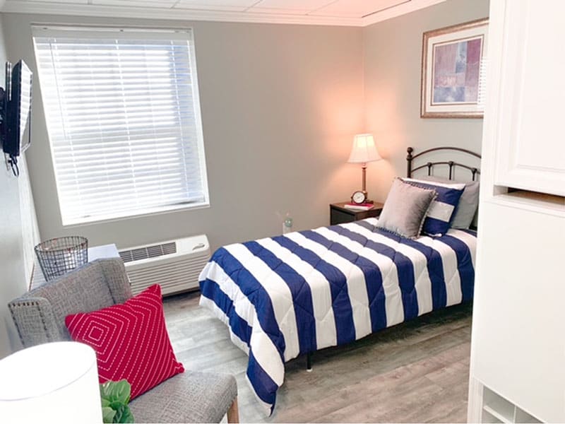 A cozy bedroom with a single bed featuring striped bedding and a bedside lamp, complemented by modern decor.