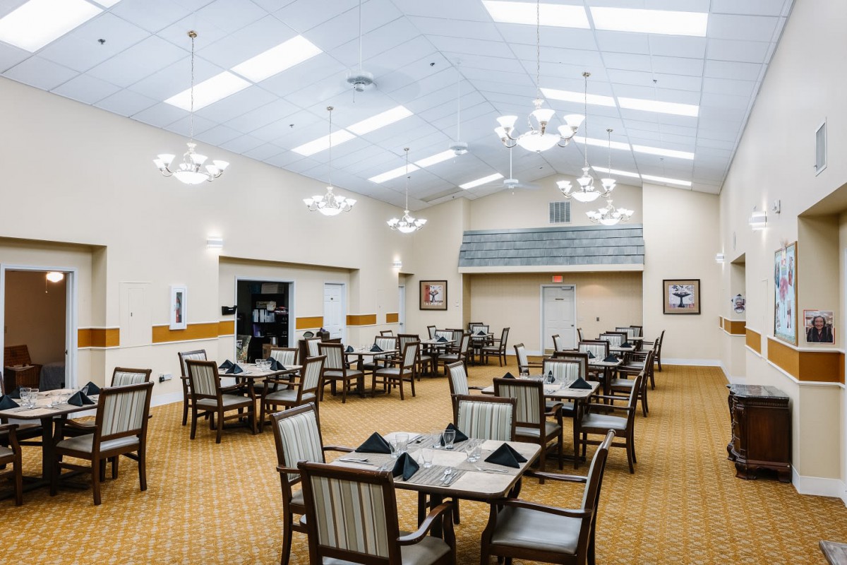 A spacious dining room with neatly arranged tables and chairs under bright ceiling lights.