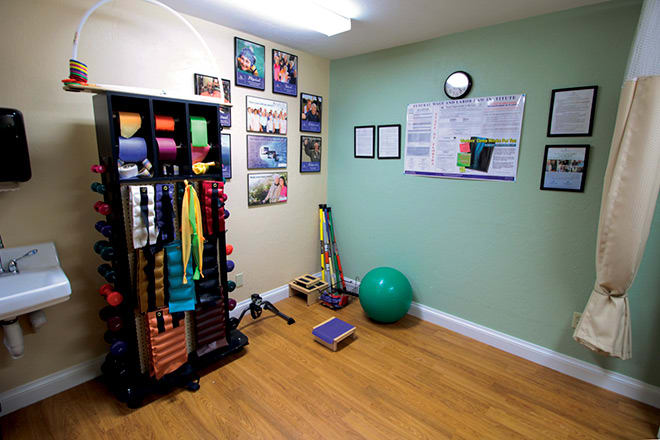 A small exercise room equipped with yoga mats, resistance bands, a stability ball, and motivational posters on the walls.