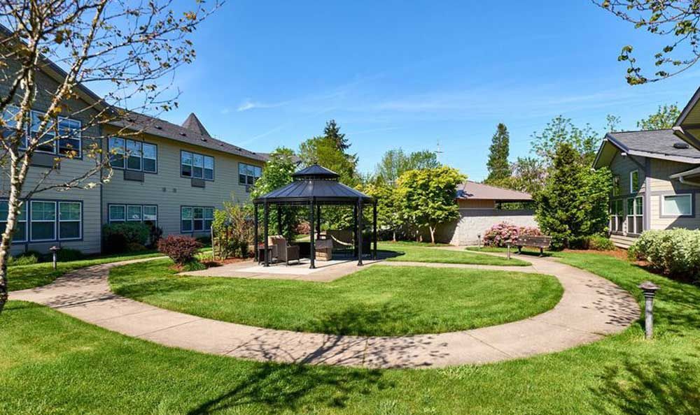 A peaceful garden with a central gazebo, surrounded by lush green lawns and trees on a sunny day.