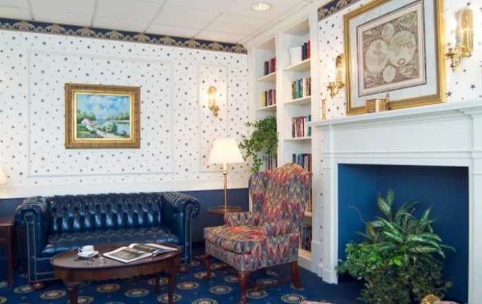 A traditionally decorated living room with a patterned armchair, bookshelf, and fireplace.
