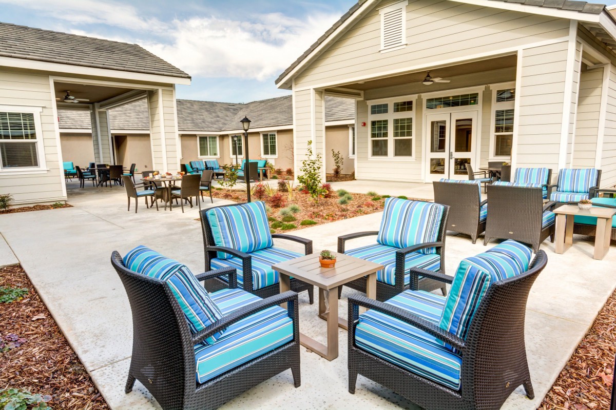A cozy outdoor patio area featuring wicker furniture with blue striped cushions, surrounded by residential buildings.