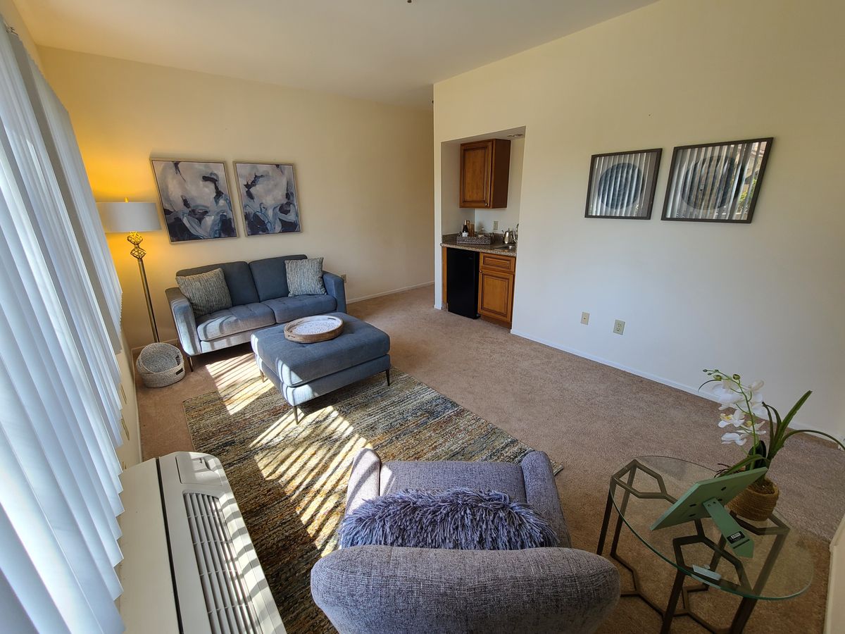 A cozy living room with a sofa, coffee table, and warm lighting from a standing lamp. Artwork decorates the walls, creating a relaxing atmosphere.
