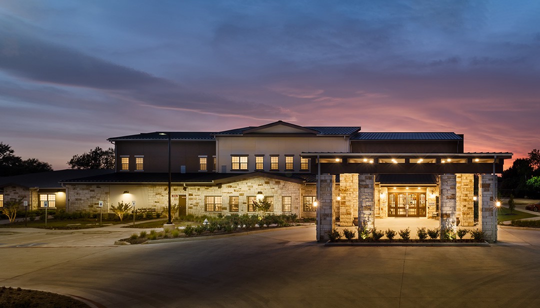 A well-lit building entrance during twilight with landscaped surroundings.