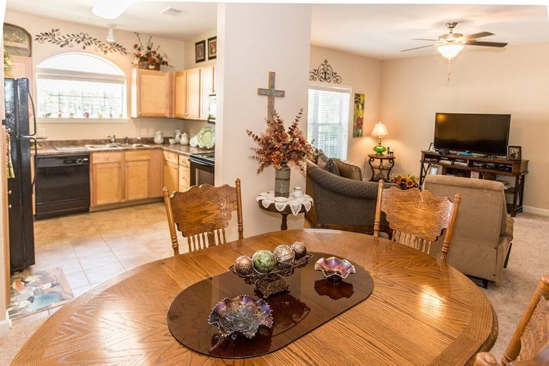 A cozy interior featuring a dining area with a wooden table, a kitchen in the background, and a living room with comfortable seating.