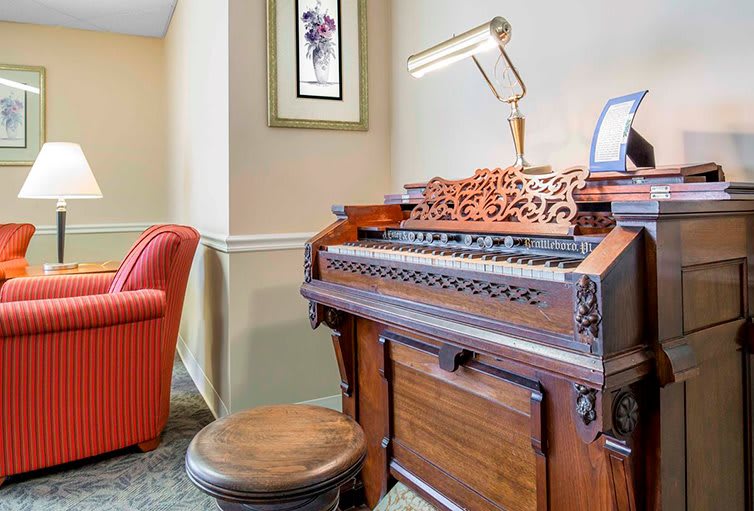 A vintage wooden organ in a cozy interior setting with a red chair and framed artwork.
