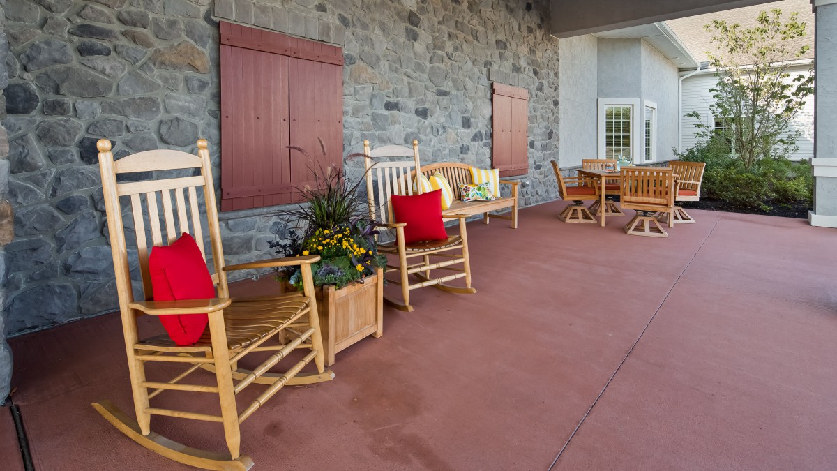 A cozy porch with wooden rocking chairs adorned with colorful cushions and a decorative planter against a stone wall.