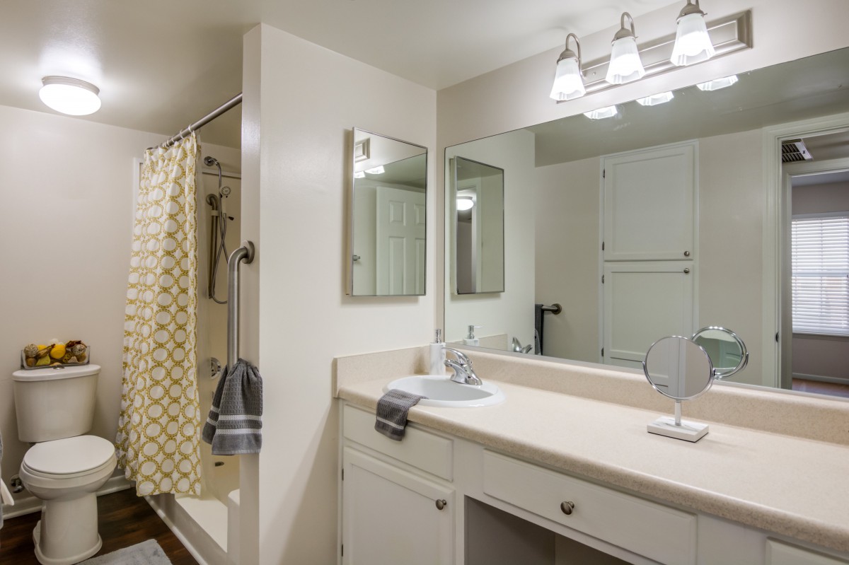 A clean and well-organized bathroom with a mirror, sink, and shower area.