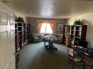 A cozy library room with bookshelves, seating, and a window providing natural light.