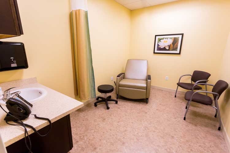 A small medical room with chairs, a stool, a curtain, and a sink.
