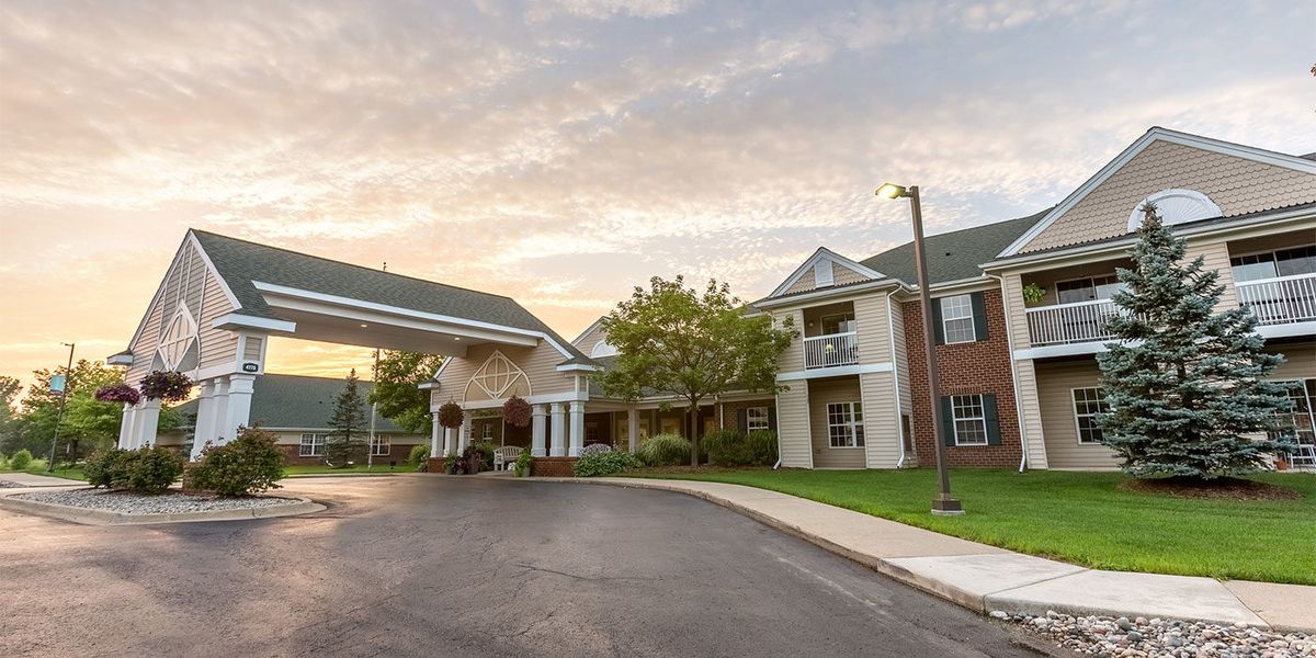 A scenic view of a large building at sunset with a driveway and surrounding greenery.