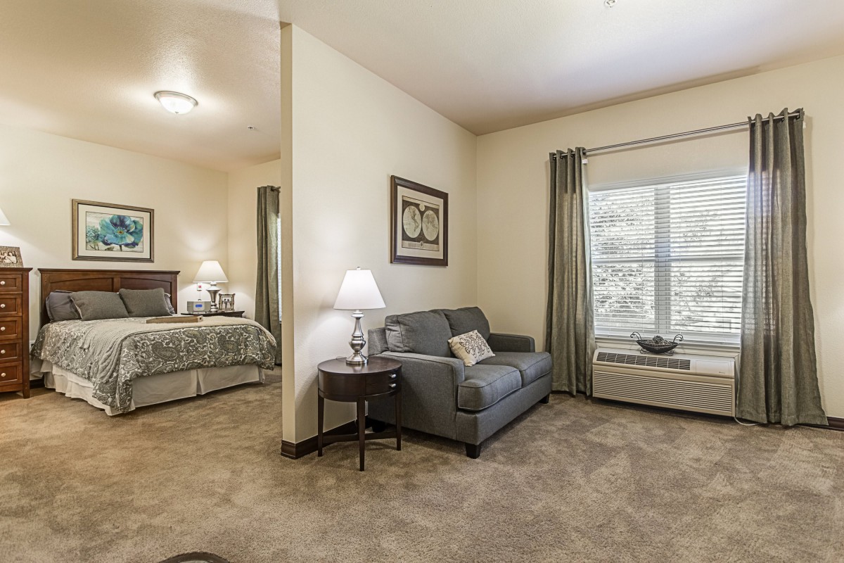A cozy apartment with a small living area, featuring a sofa and lamp, adjacent to a bedroom.