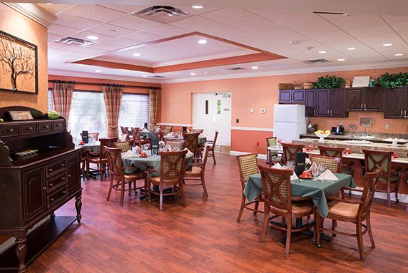 A cozy dining room with neatly arranged tables and chairs, featuring wooden floors and large windows.