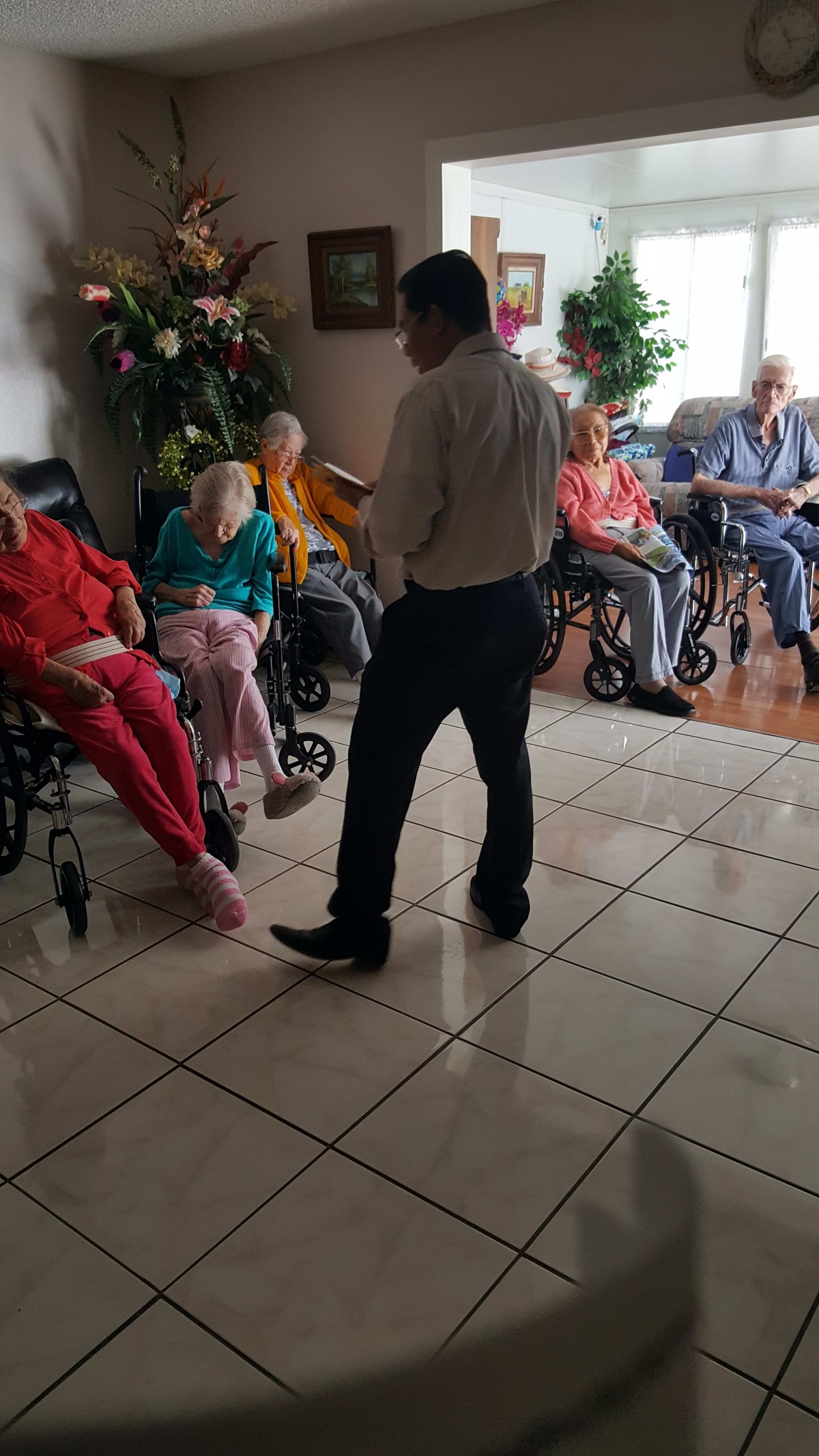 A group of elderly people in wheelchairs being attended to in a nursing home setting.