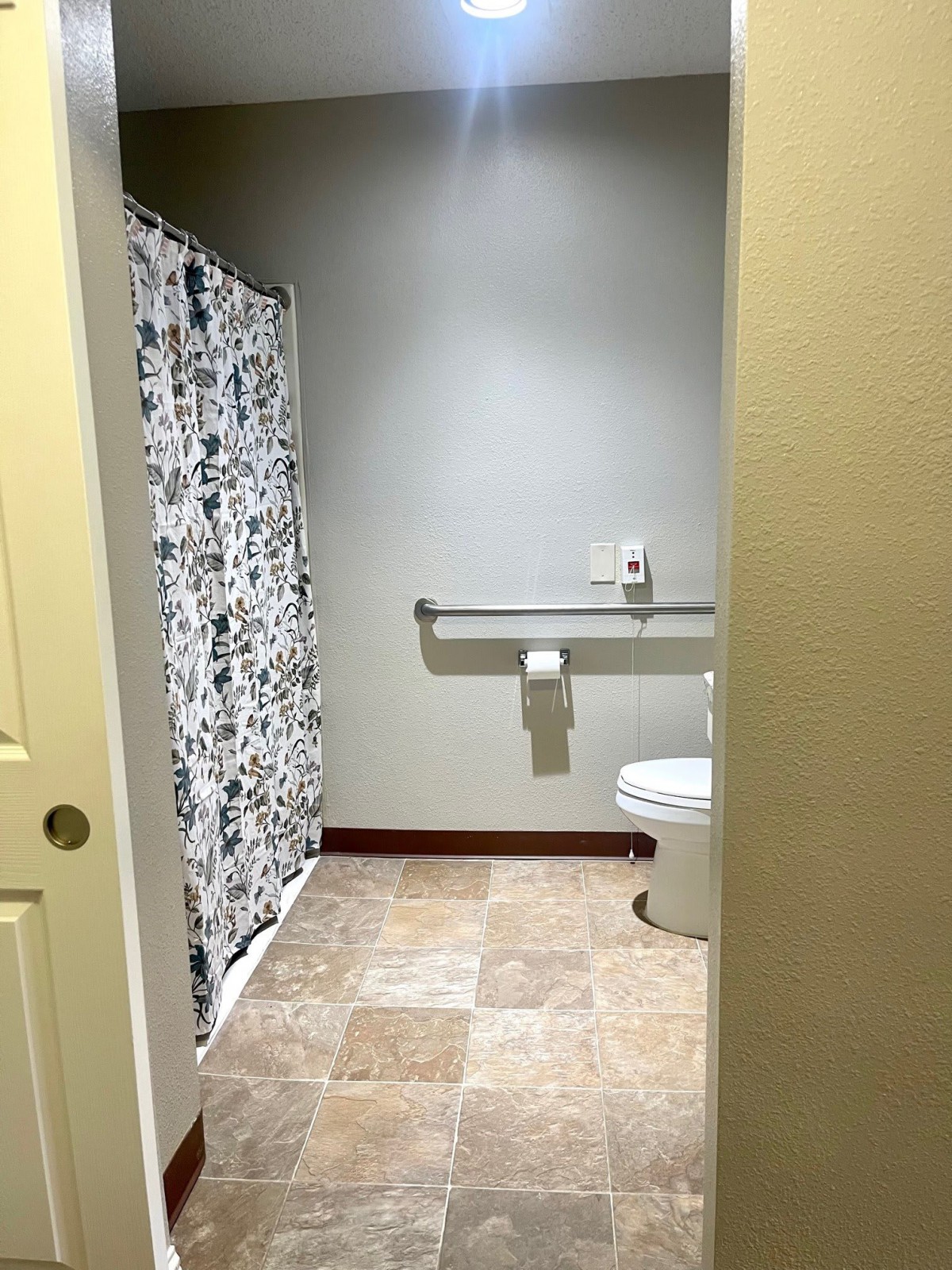 A bathroom with a toilet, shower, and grab bar for accessibility.