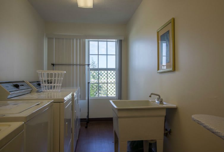 A bright and tidy laundry room with a washing machine, sink, and a window.