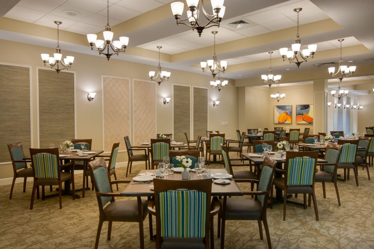 A well-lit dining room with neatly arranged tables and chairs, adorned with elegant chandeliers.