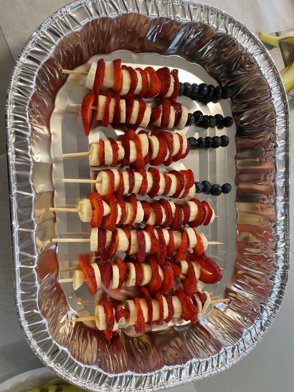 Fruit skewers with strawberries, bananas, and blueberries arranged in a foil tray.