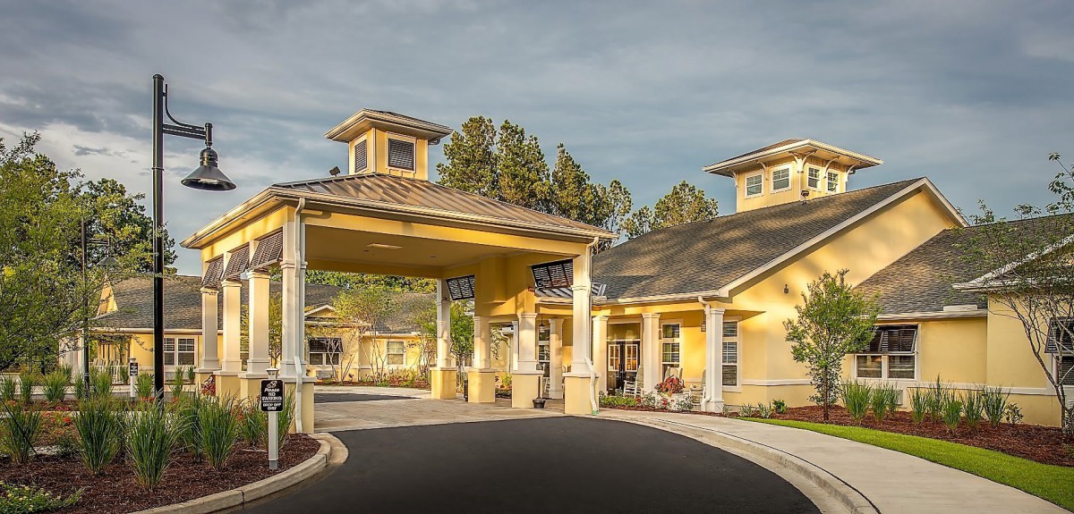 A yellow residential building with a covered entrance and landscaped surroundings.