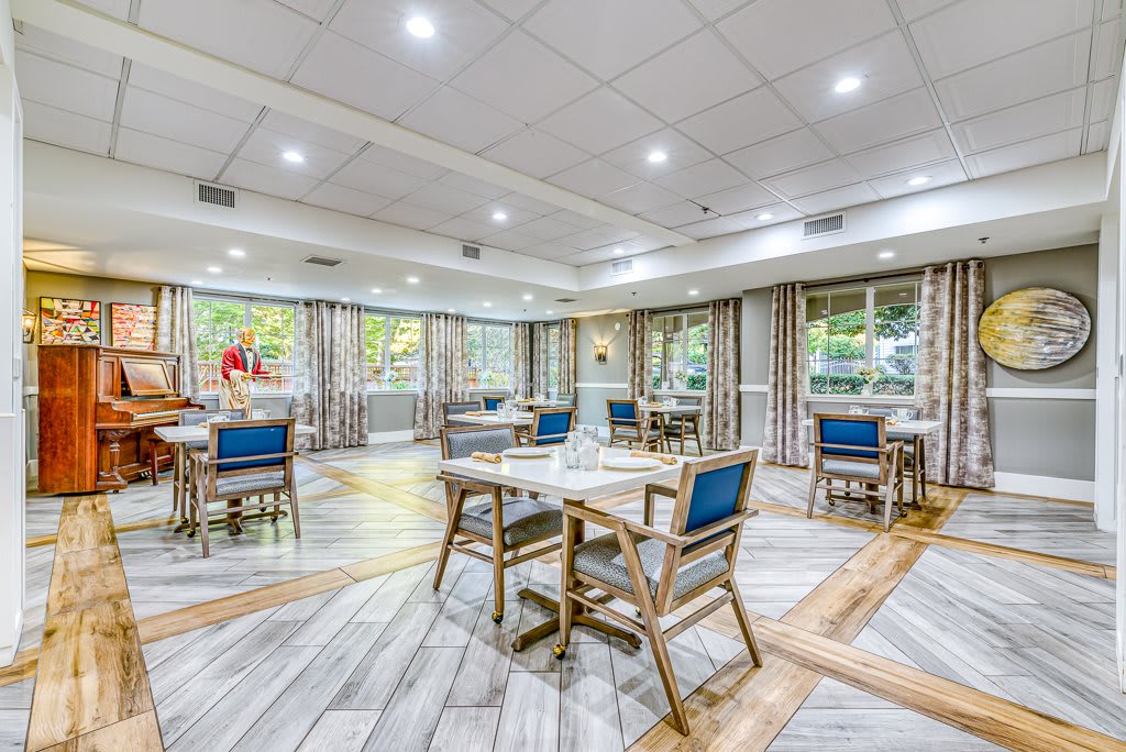 A modern dining room interior with neatly arranged tables and chairs, well-lit with ample natural light coming through large windows.