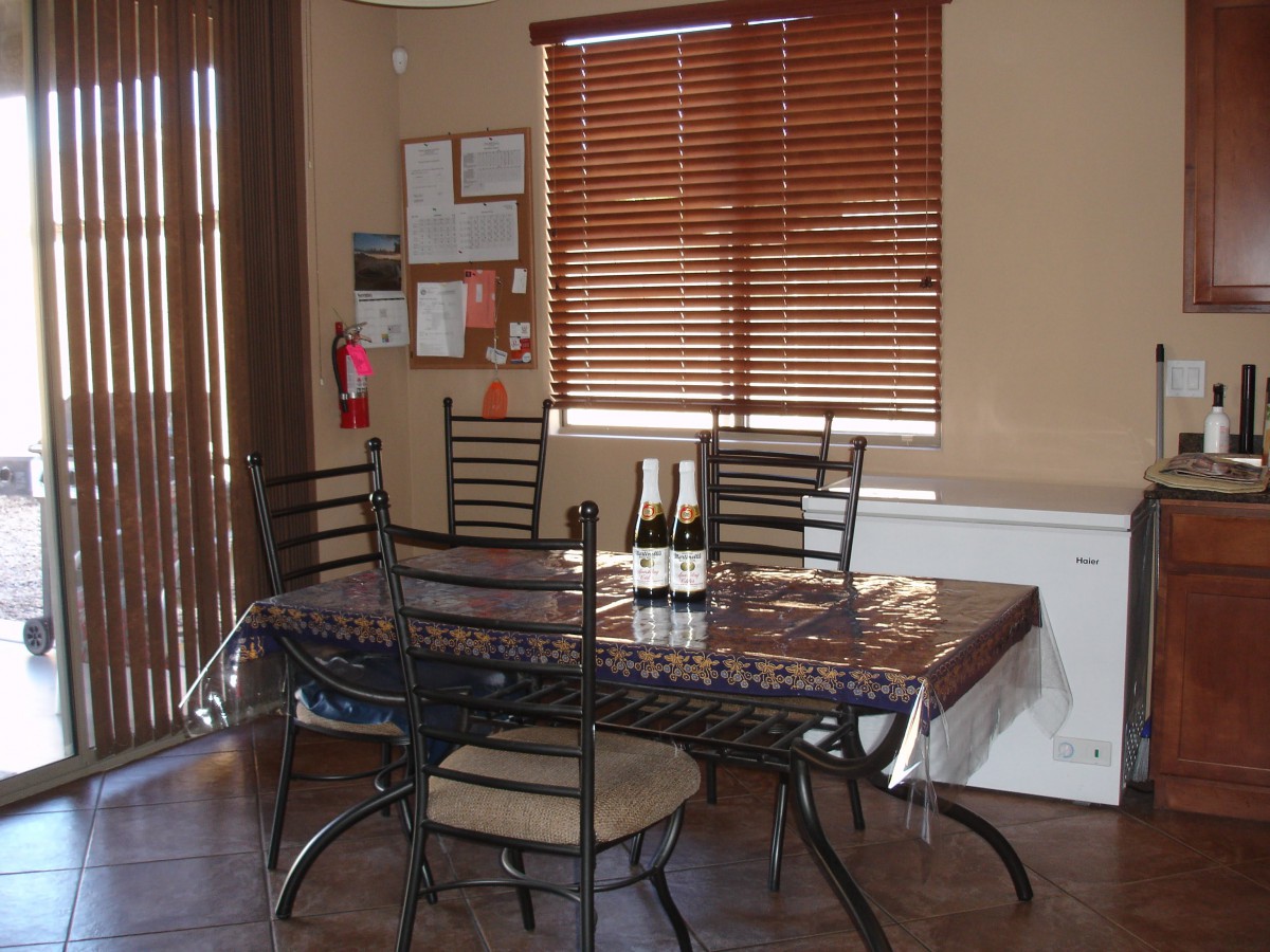 A dining room with a table and chairs, featuring wine bottles and window blinds.