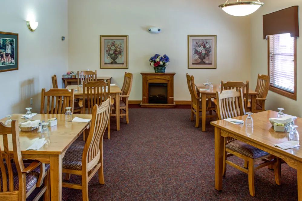 A cozy dining room with wooden tables and chairs, decorated with framed art and a floral arrangement.