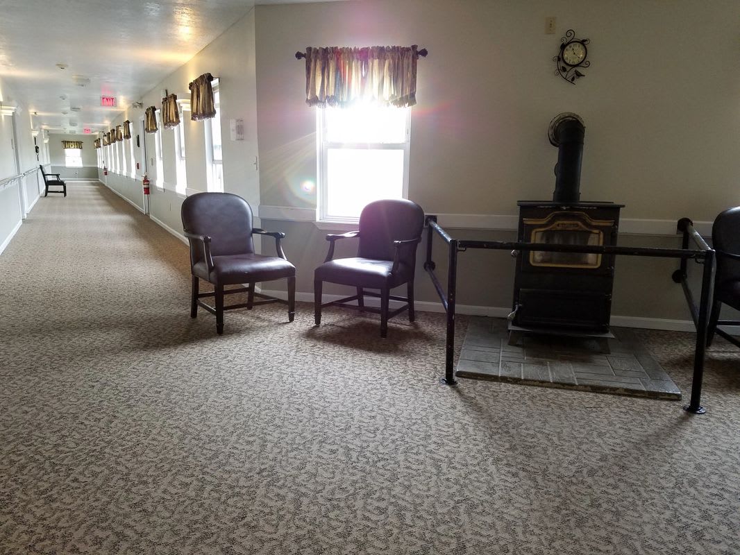 A quiet hallway featuring two chairs, a window with curtains, and carpeted flooring.