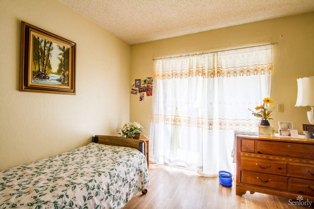 A cozy bedroom with a single bed, floral bedding, and natural light streaming through the curtains.