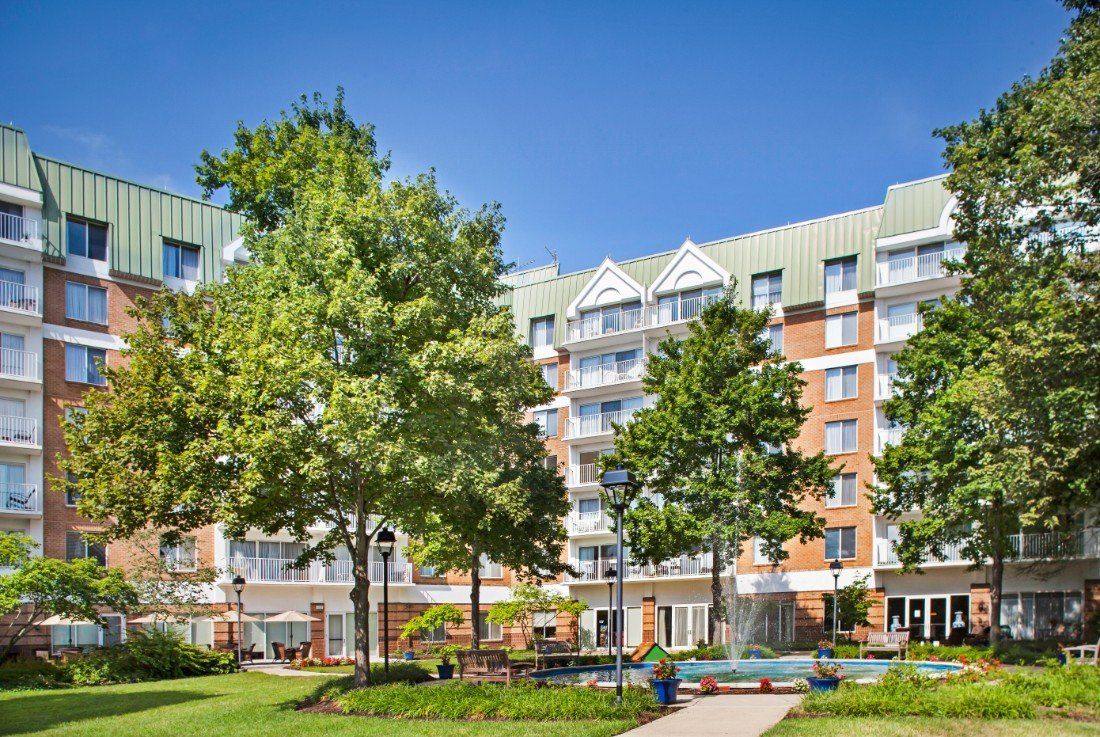 A residential apartment building surrounded by trees and a park-like outdoor area.