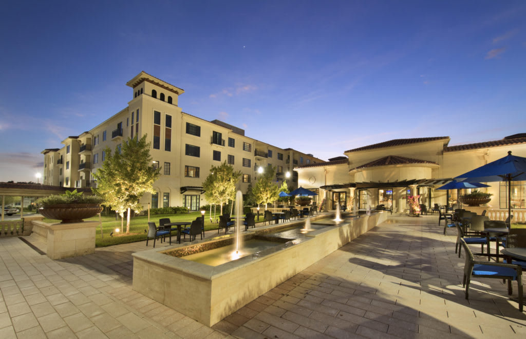Evening view of a beautifully lit building with fountains and trees.