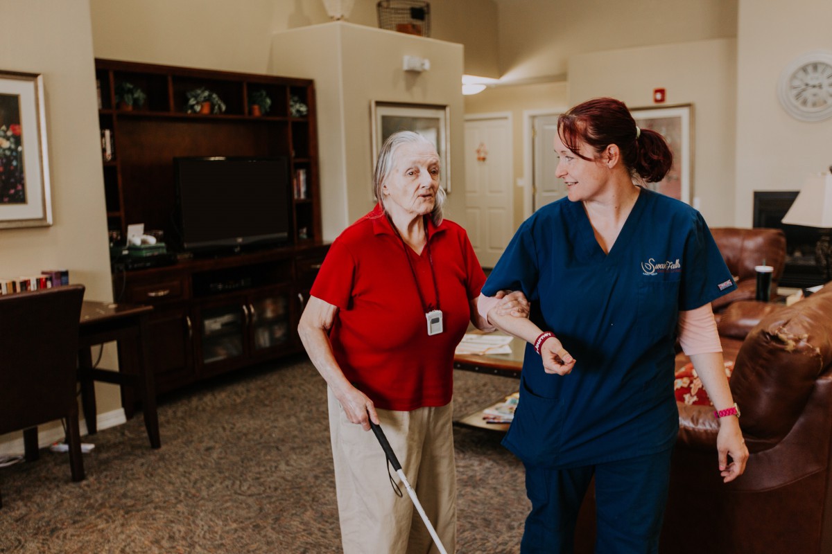 A caregiver assisting an elderly person with walking indoors.