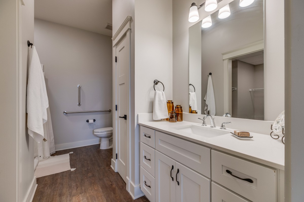 A modern bathroom with a double sink, large mirror, and sleek cabinetry, featuring bright lighting and a visible toilet area.