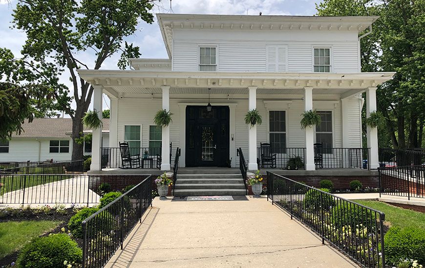 A white house with a porch and columns, featuring hanging plants and an inviting entrance.