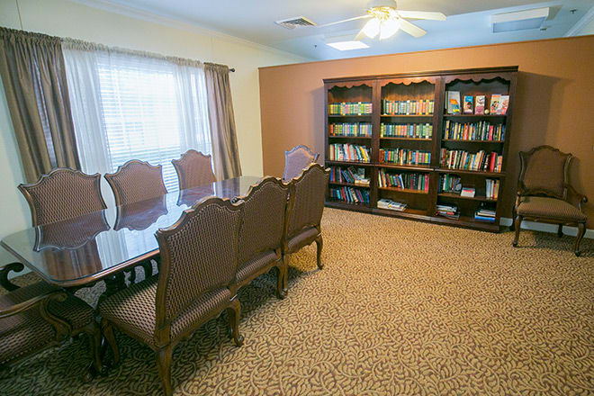 A cozy library and meeting room featuring a large table, chairs, and wall-to-wall bookshelves filled with books.