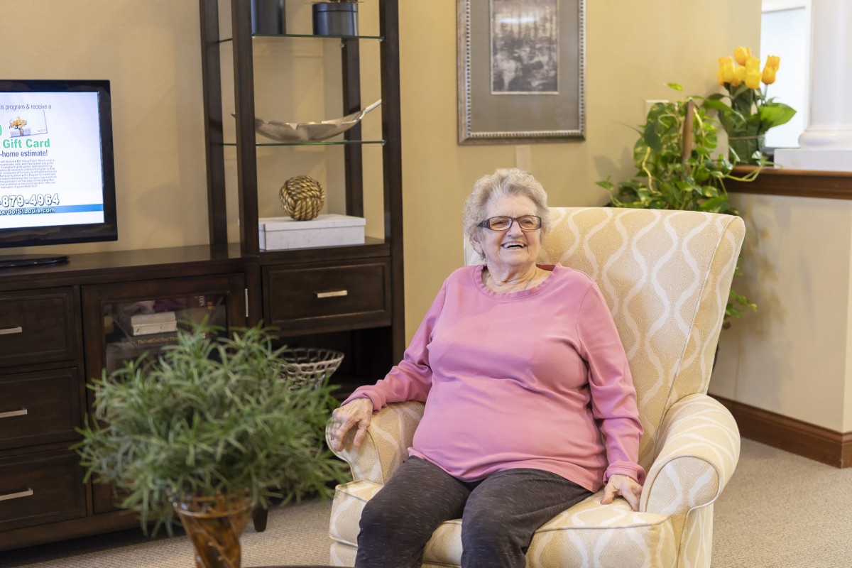 An elderly woman sitting comfortably in an armchair in a cozy living room setting.