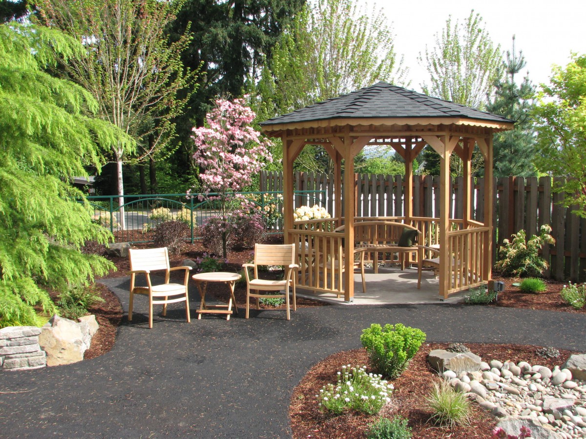 A tranquil garden setting featuring a wooden gazebo surrounded by lush greenery and chairs for relaxation.