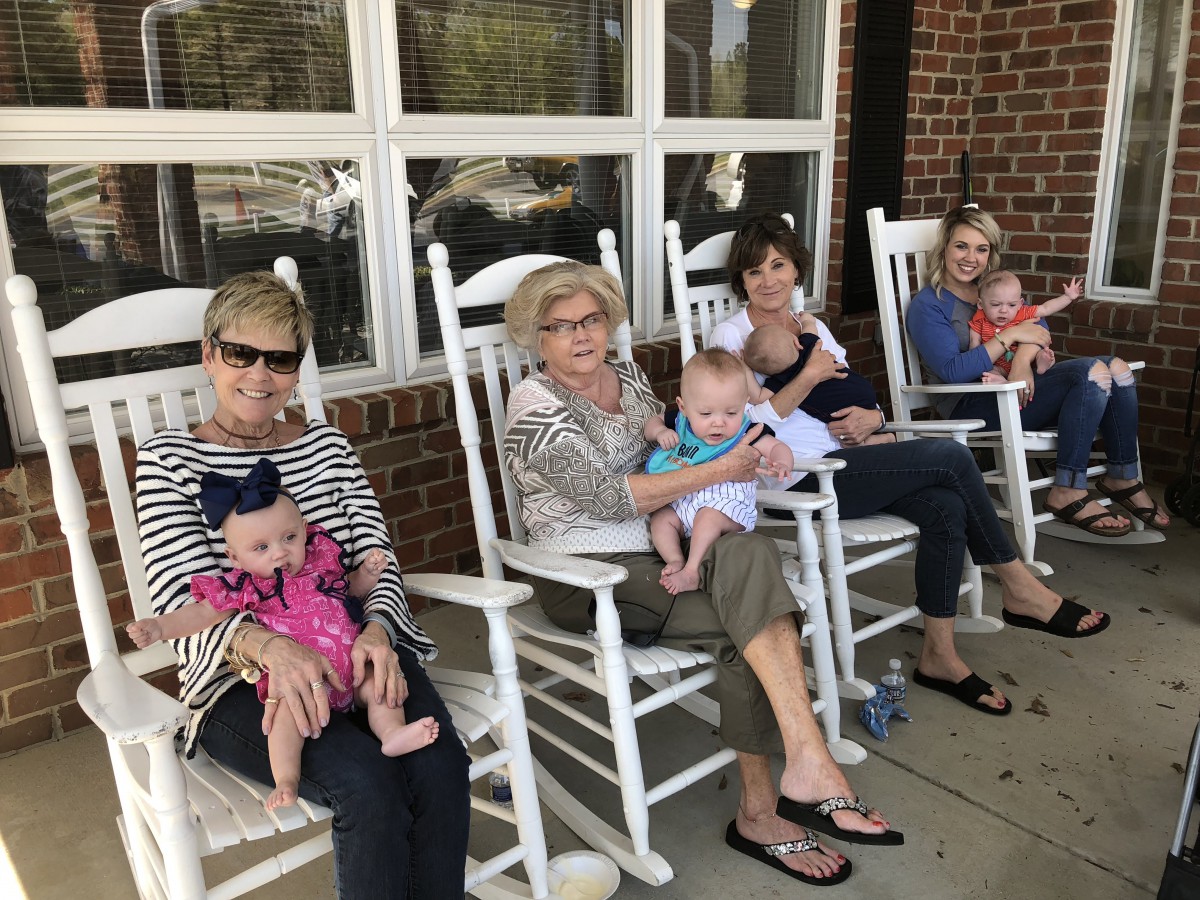 A group of women sitting on a porch in rocking chairs, each holding a baby.