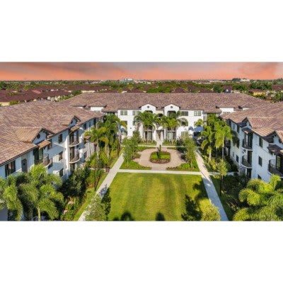Aerial view of a residential building complex with landscaped gardens and palm trees under a sunset sky.