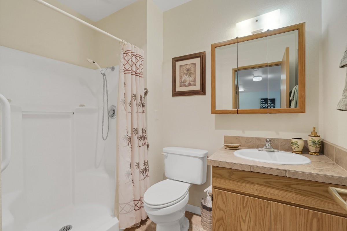 A clean and simple bathroom with a shower, toilet, sink, and mirror.